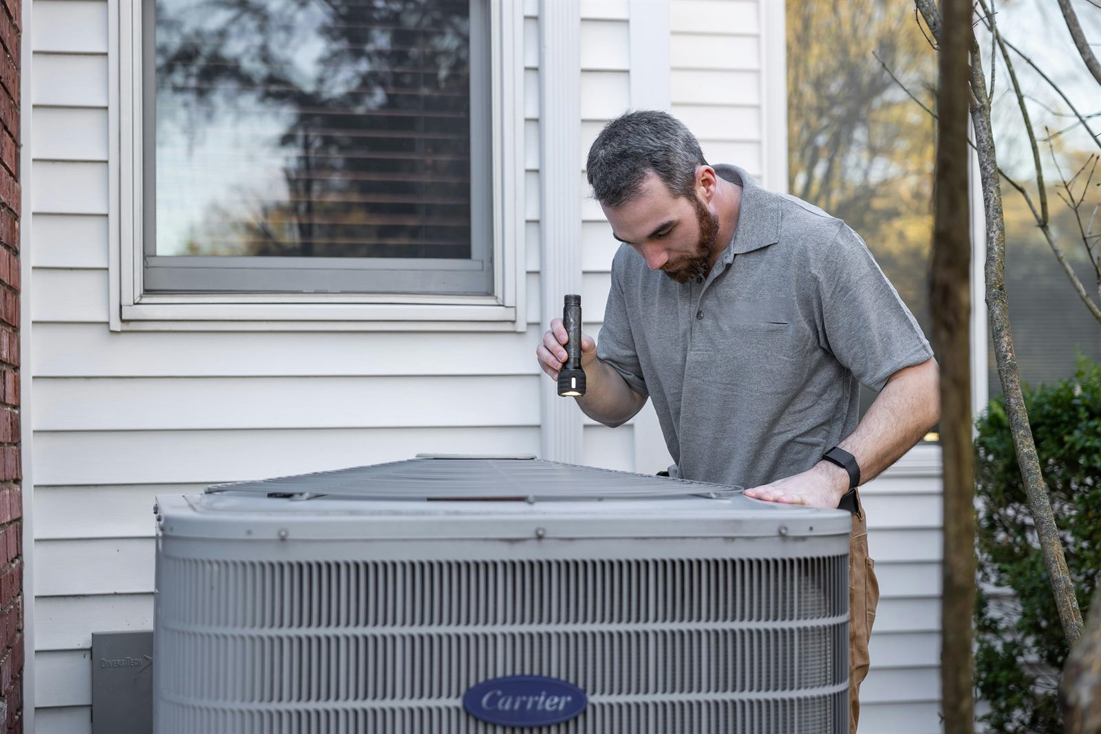 HVAC repair technician inspecting a Carrier air conditioner condenser at a Columbus OH home